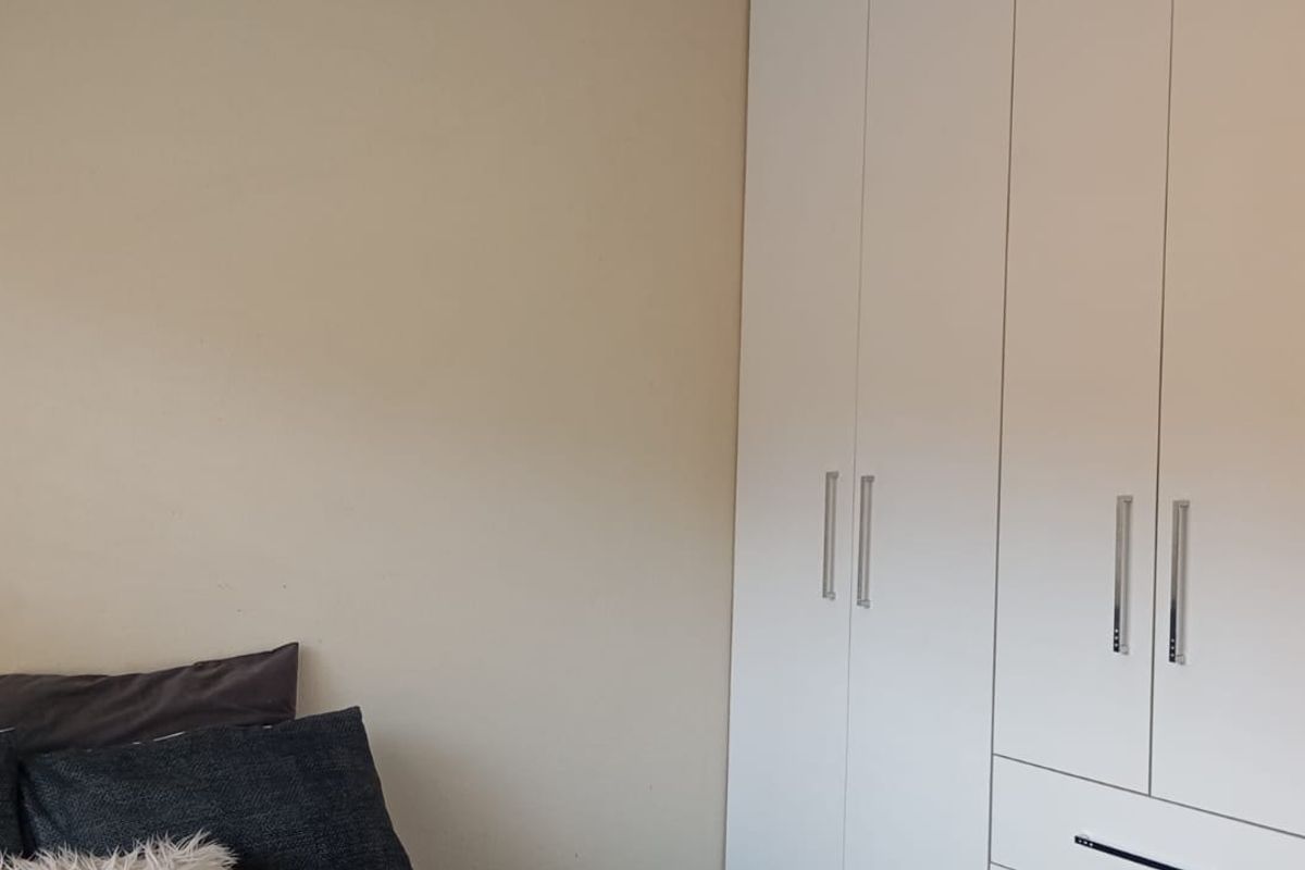 A bedroom featuring built-in floor-to-ceiling white cabinetry with modern silver handles, providing ample storage space.