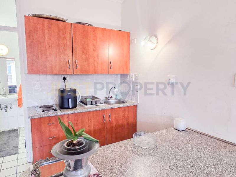 Compact kitchen featuring laminate cabinetry, granite countertops, and an integrated electric hob, with an adjacent bathroom visible through the doorway.