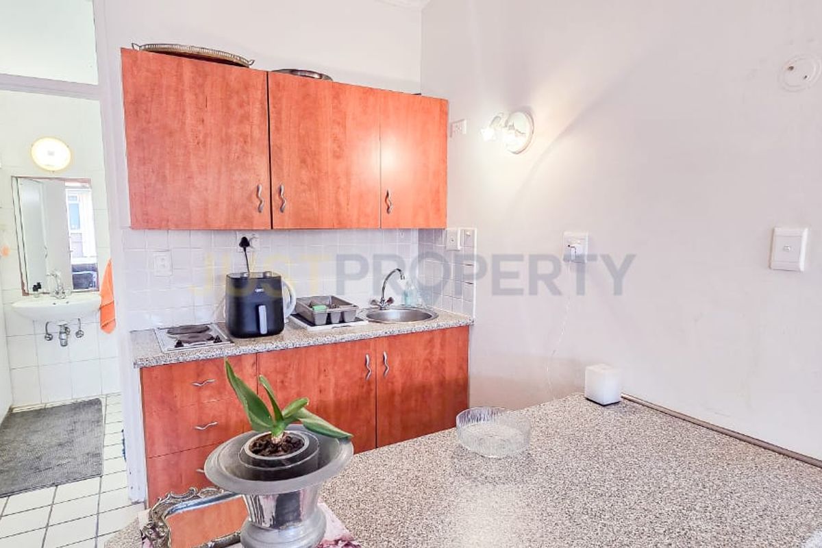 Compact kitchen featuring laminate cabinetry, granite countertops, and an integrated electric hob, with an adjacent bathroom visible through the doorway.