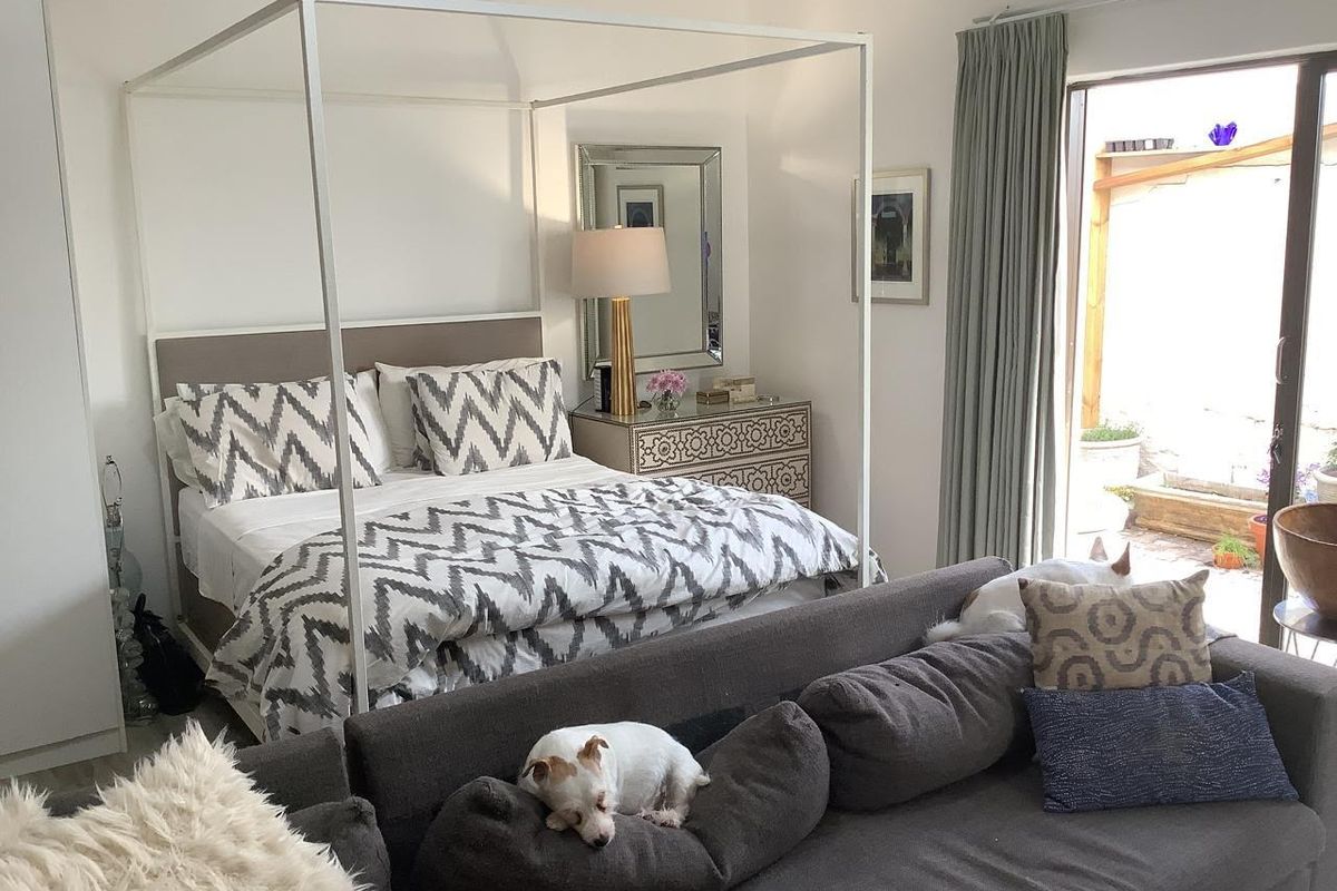 A bright bedroom featuring a four-poster bed frame, built-in wardrobe, and direct access to an outdoor patio area through a sliding glass door.