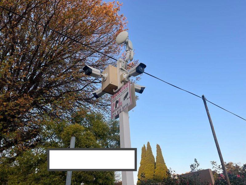 A security pole equipped with multiple CCTV cameras and a security warning sign.