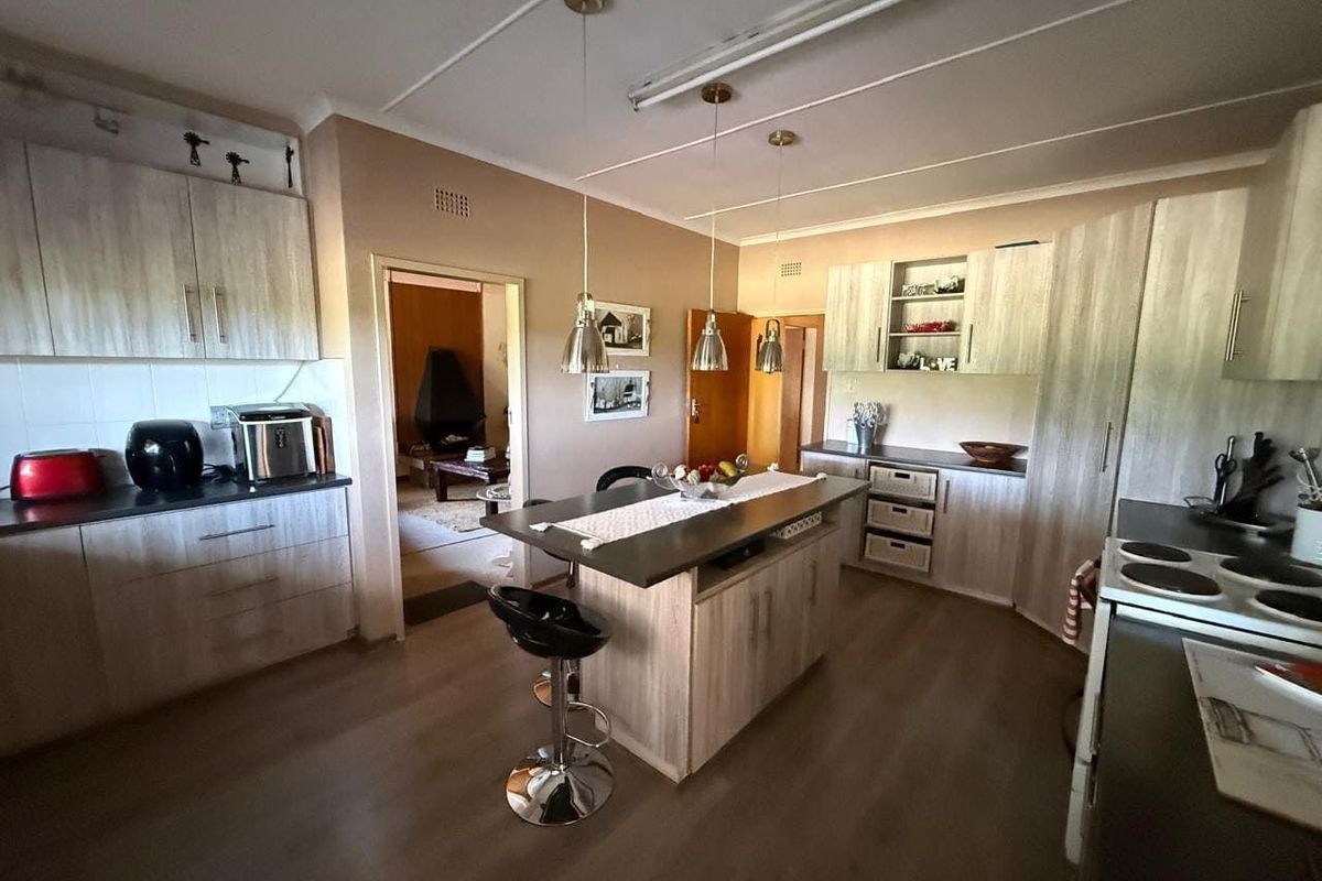 A functional kitchen featuring light wood-grain cabinetry, a central island with breakfast bar seating, and integrated lighting, connecting to an adjacent living area.