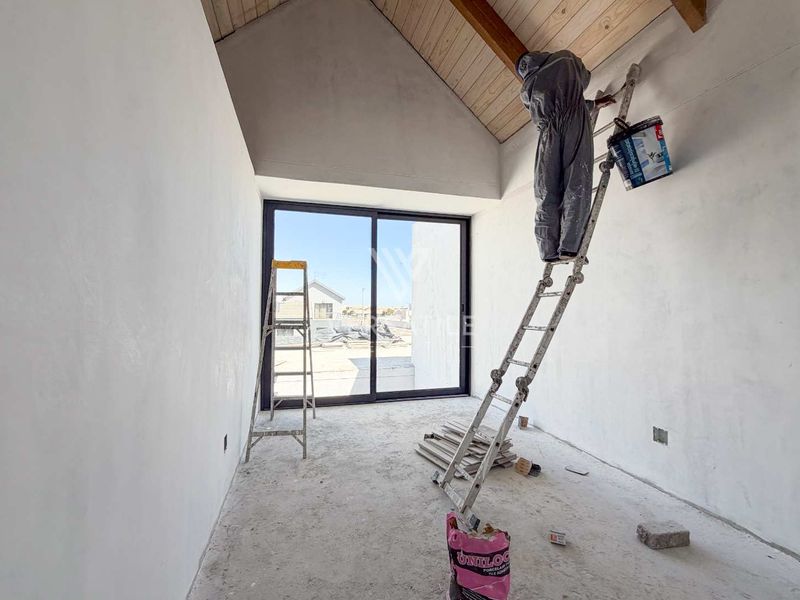 An unfinished bedroom interior featuring a high vaulted timber ceiling and large sliding glass doors, currently undergoing construction and painting.