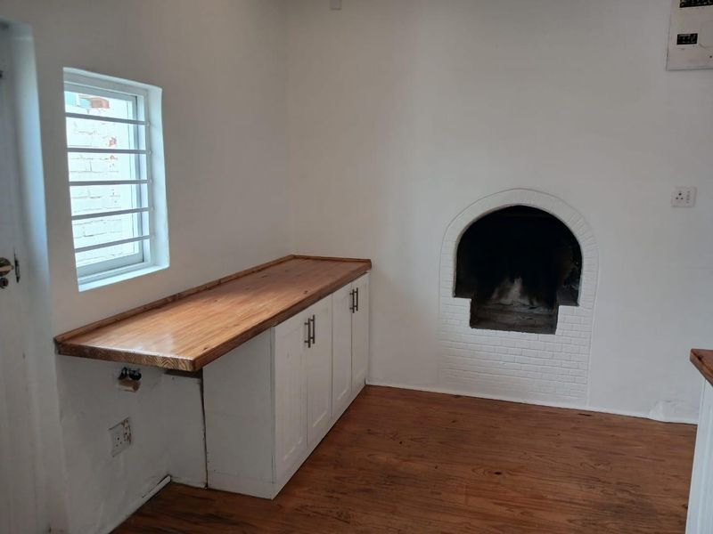 A bright kitchen area featuring built-in white cabinetry with a wooden countertop, timber flooring, and a traditional arched built-in fireplace.