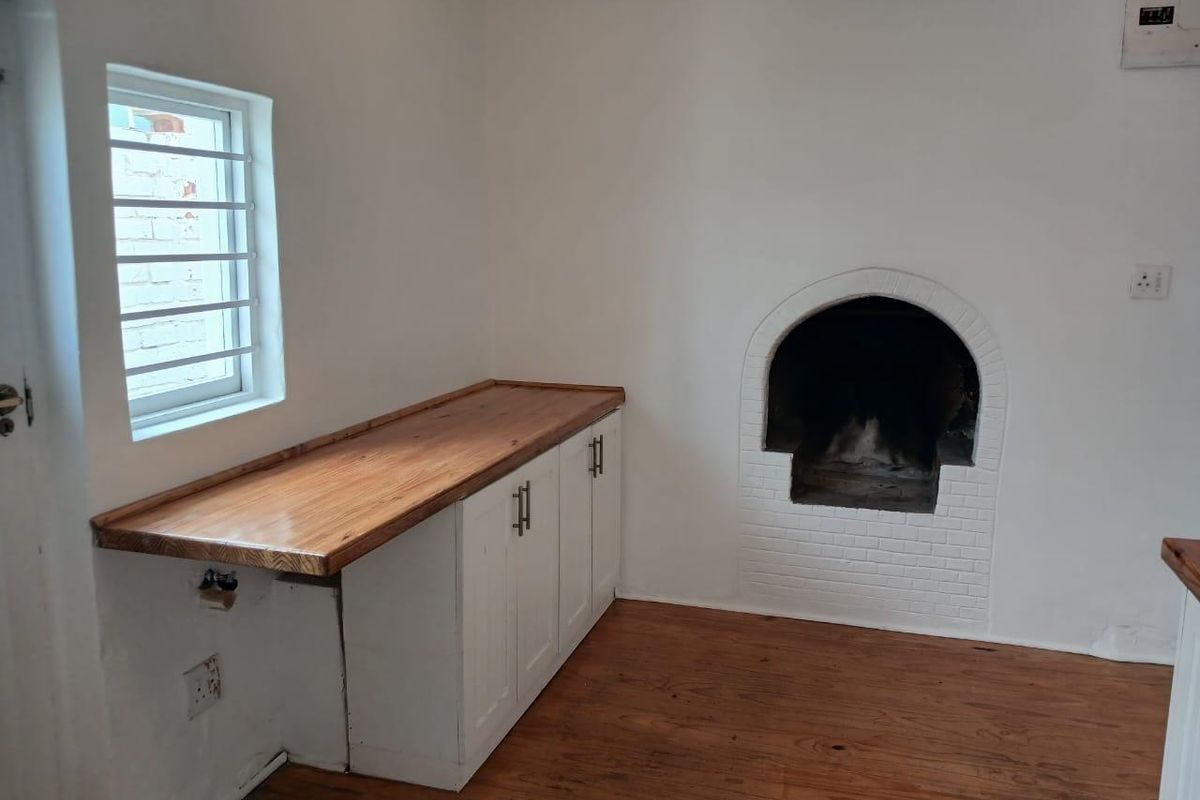 A bright kitchen area featuring built-in white cabinetry with a wooden countertop, timber flooring, and a traditional arched built-in fireplace.