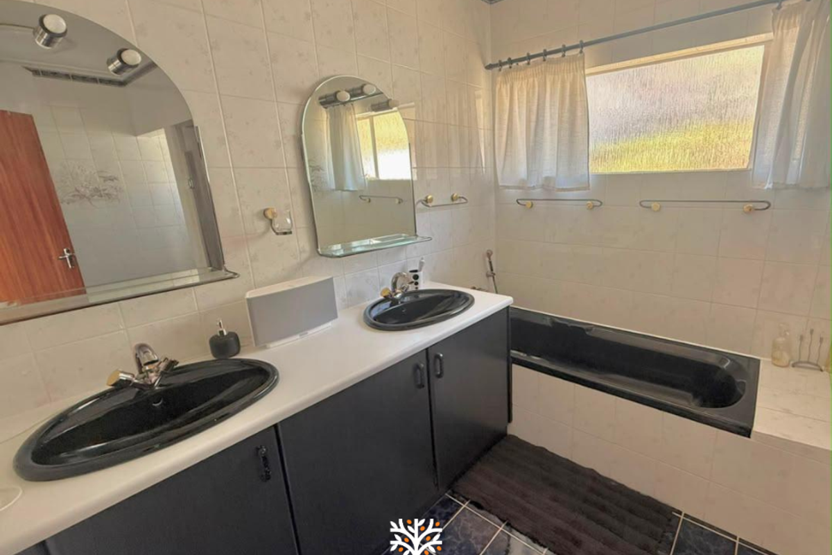 A functional bathroom featuring a double vanity with black basins, a built-in bathtub, and tiled finishes throughout.