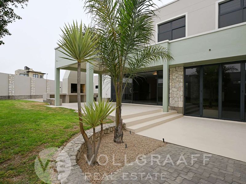 Rear view of the property featuring a covered patio with a built-in braai, stone cladding accents, and large sliding glass doors leading to the interior.