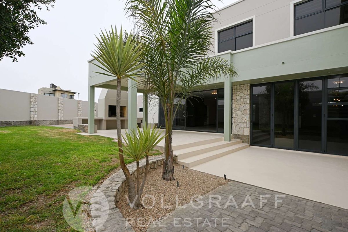 Rear view of the property featuring a covered patio with a built-in braai, stone cladding accents, and large sliding glass doors leading to the interior.