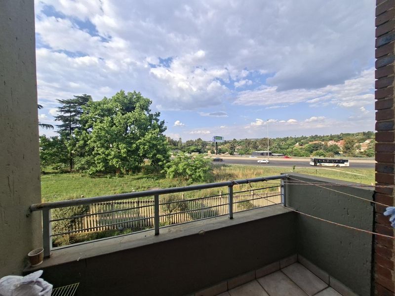 A balcony featuring tiled flooring and a metal balustrade, offering an open view of the surrounding landscape and nearby road.