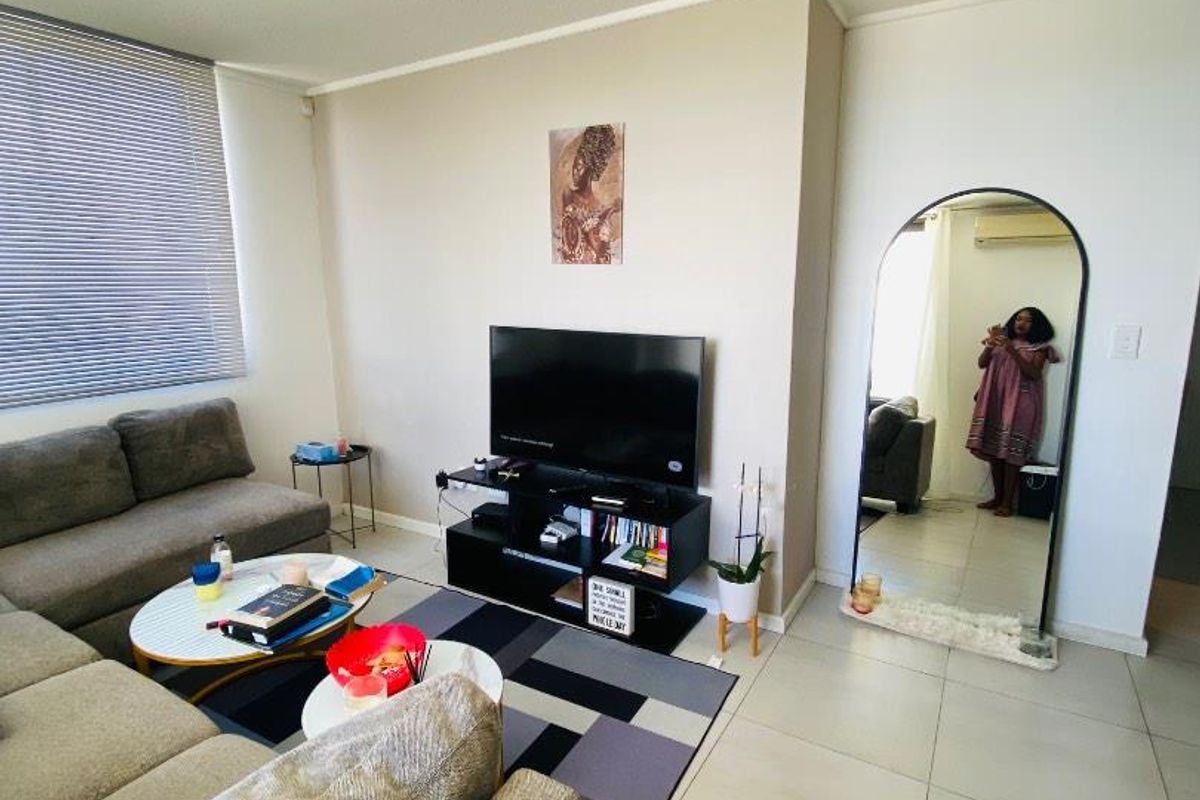 A bright living room featuring large format floor tiles, a modern track lighting fixture, and a window fitted with horizontal blinds.
