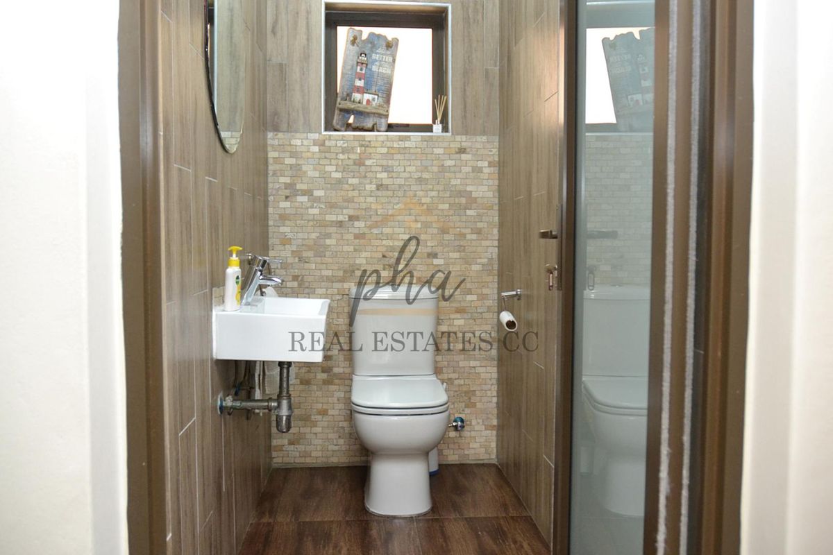 A compact, modern bathroom featuring wood-look floor and wall tiles, a wall-mounted basin, and a mosaic-tiled feature wall behind the toilet.