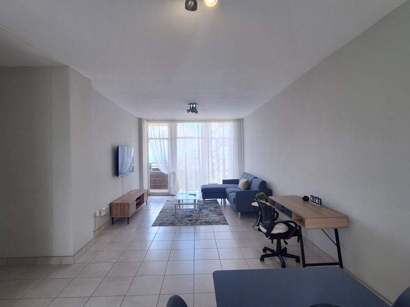 A spacious living room featuring neutral tiled flooring and large sliding glass doors that provide ample natural light and access to the balcony.