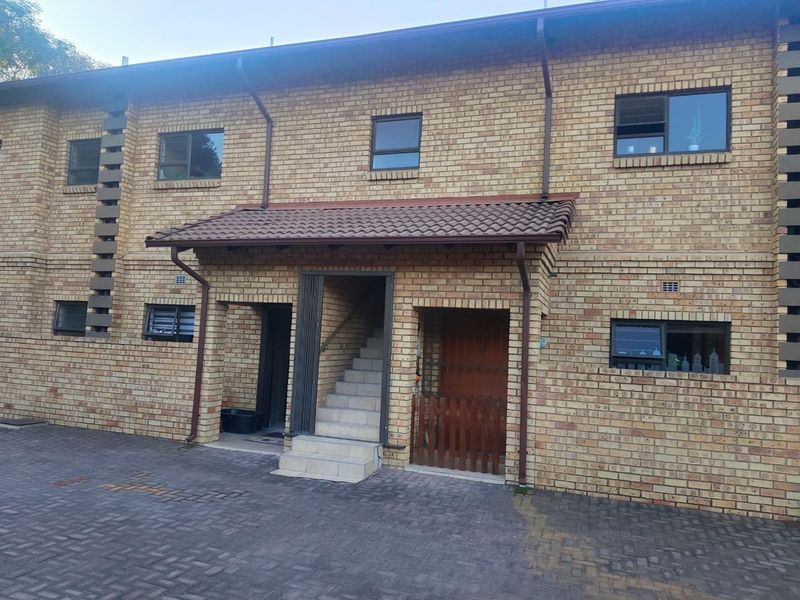 Front elevation of a face brick townhouse featuring a paved driveway, external staircase, and tiled roof entrance canopy.