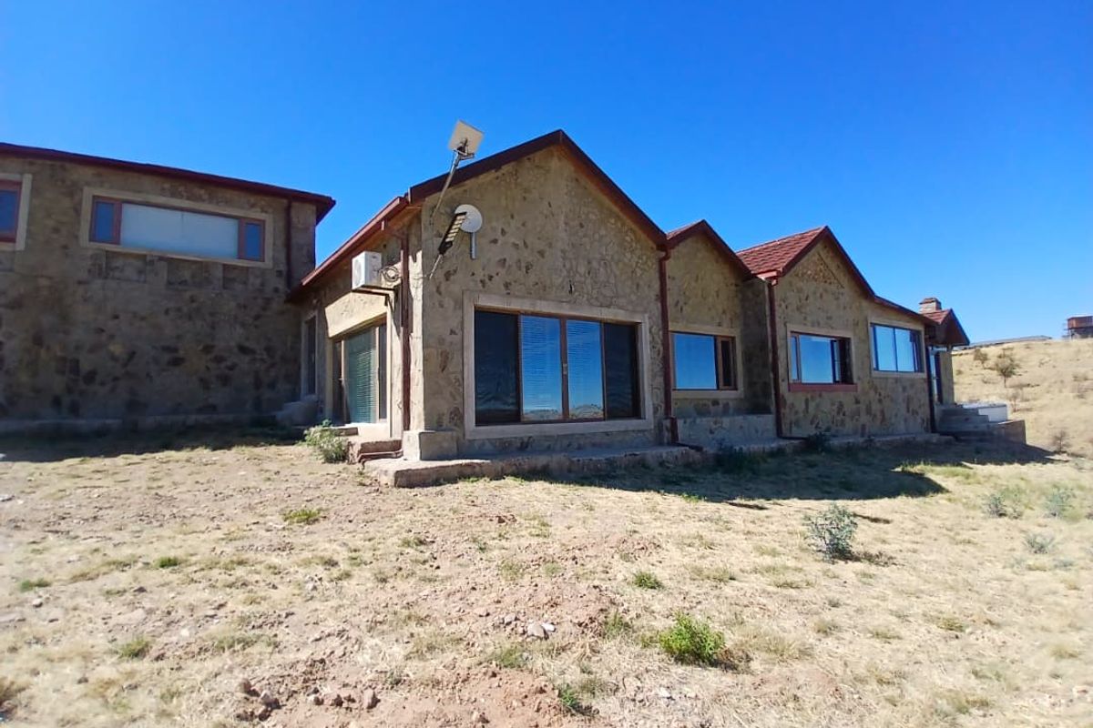 Rear view of a stone-clad small holding featuring multiple sliding glass doors, tiled roofing, and an installed air conditioning unit.