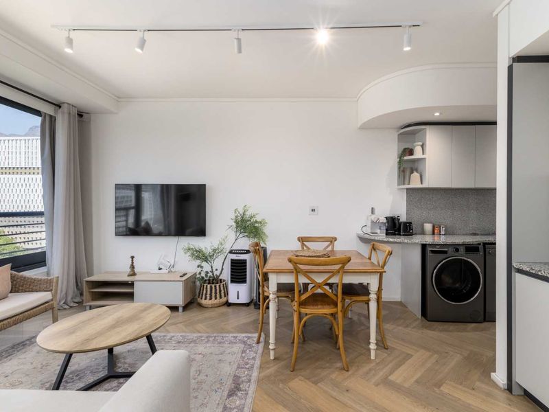 Modern open-plan living area featuring elegant herringbone timber flooring, track lighting, and a compact kitchen space with granite countertops and integrated laundry facilities.