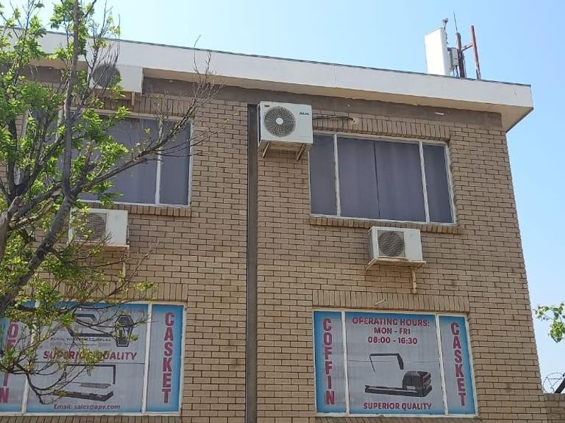 Exterior view of a two-story brick office building featuring multiple wall-mounted air conditioning units and large windows with security screens.