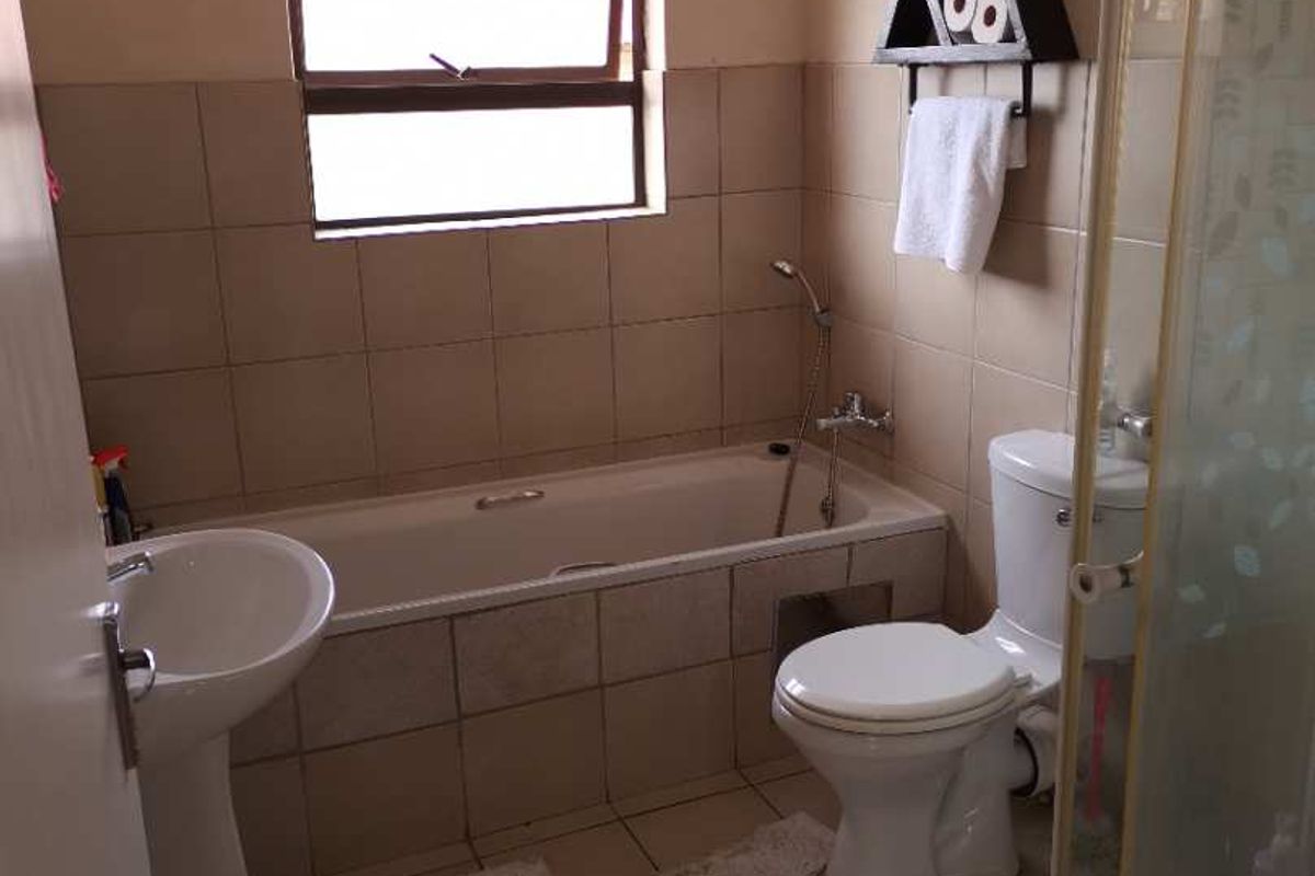 A functional bathroom featuring a pedestal basin, a bathtub with a shower mixer, and a separate shower enclosure with tiled walls and flooring.