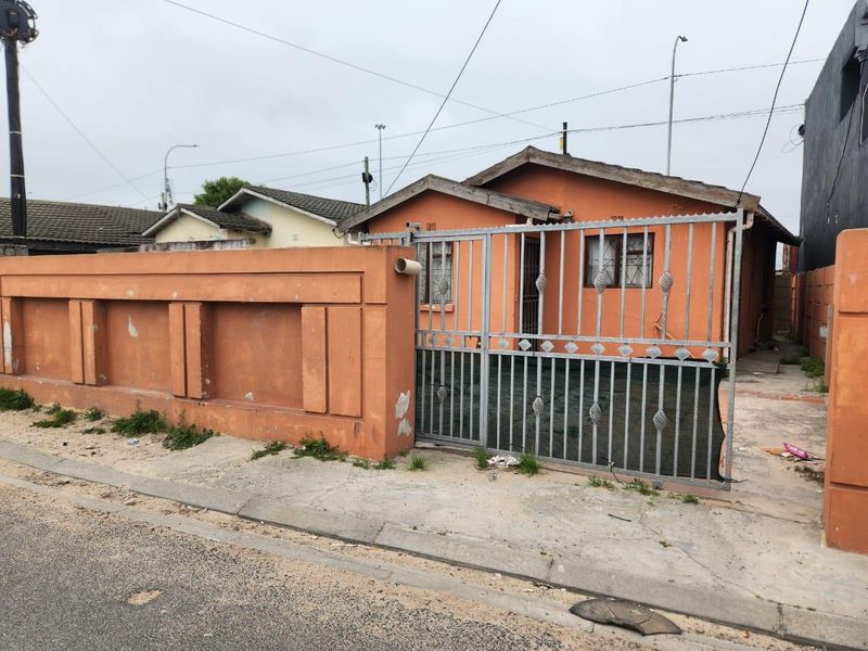 Front view of a single-story house featuring a perimeter wall, metal security gate, and tiled roof, showing signs of exterior wear.