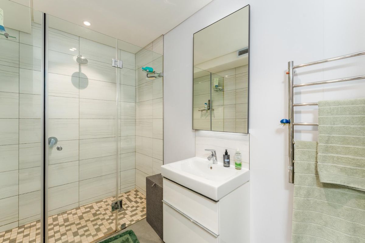 Modern bathroom featuring a glass-enclosed walk-in shower with mosaic floor tiling, a wall-mounted vanity with basin, and a heated towel rail.