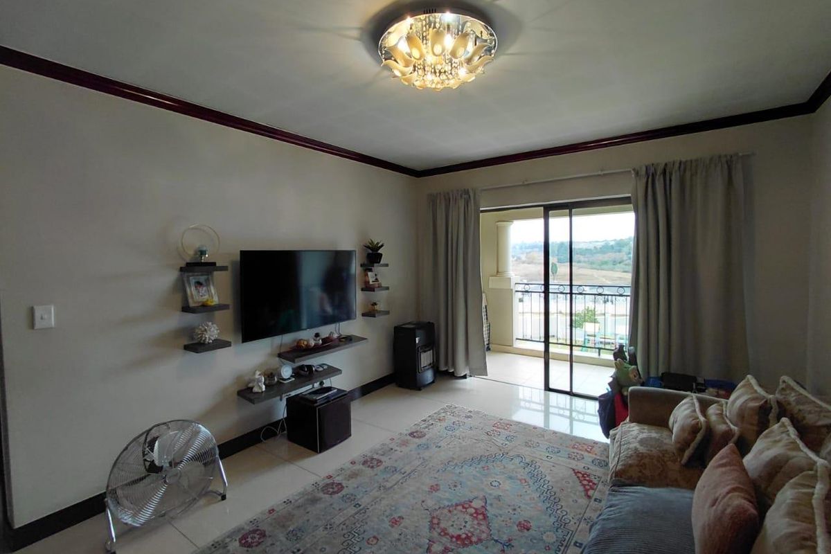 A living room featuring tiled flooring, a decorative ceiling light fixture, and sliding glass doors that open onto a balcony with outdoor views.