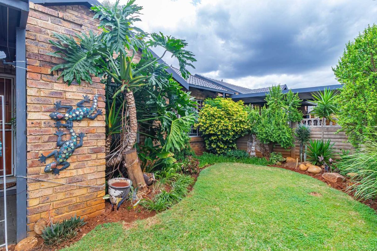 A well-maintained rear garden area featuring established landscaping, a brick facade, and a covered patio section.