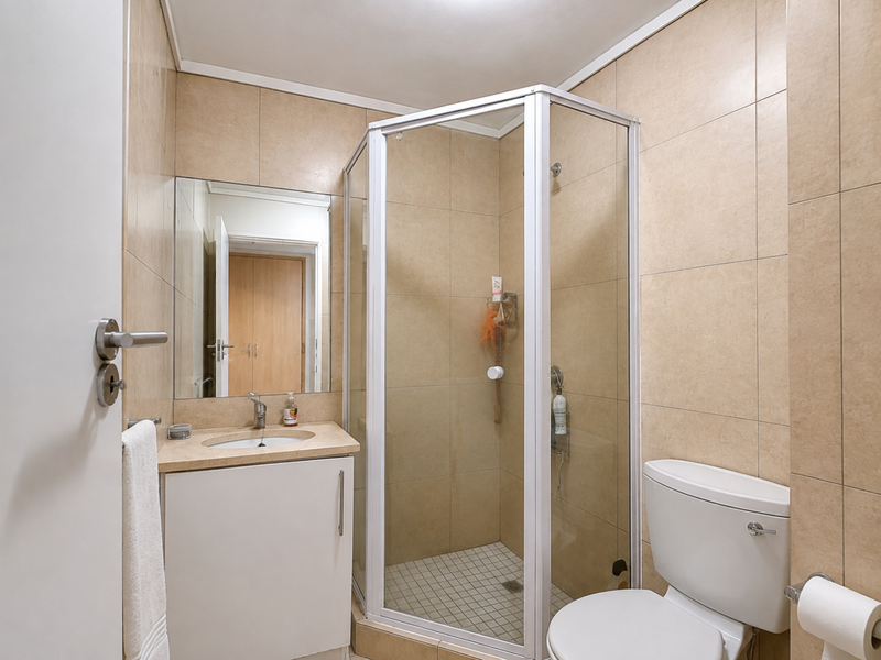 A functional bathroom featuring a corner shower enclosure, a vanity unit with an integrated basin, and neutral wall tiling.