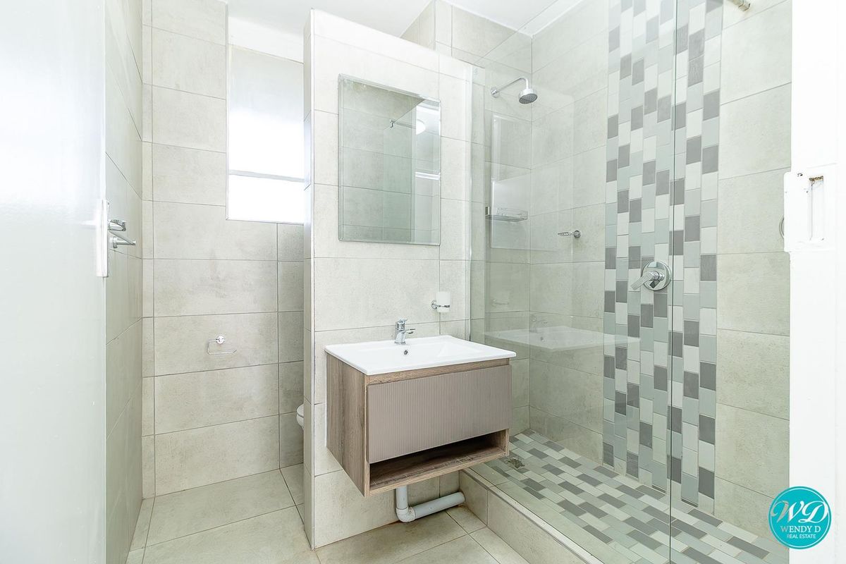 Modern bathroom featuring a glass-enclosed shower with mosaic tile accents and a wall-mounted vanity unit with neutral ceramic tiling throughout.