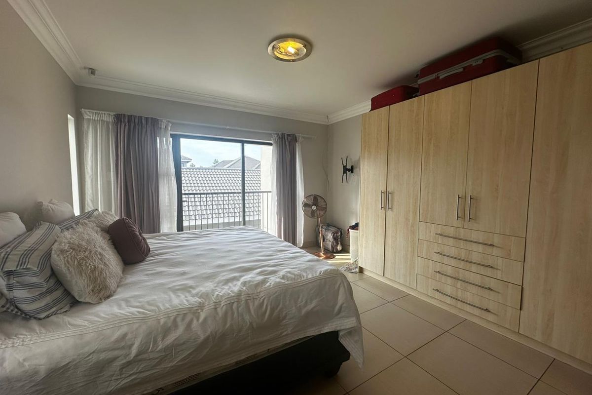 A well-lit bedroom featuring built-in light wood cabinetry, tiled flooring, and sliding glass doors leading to a private balcony.