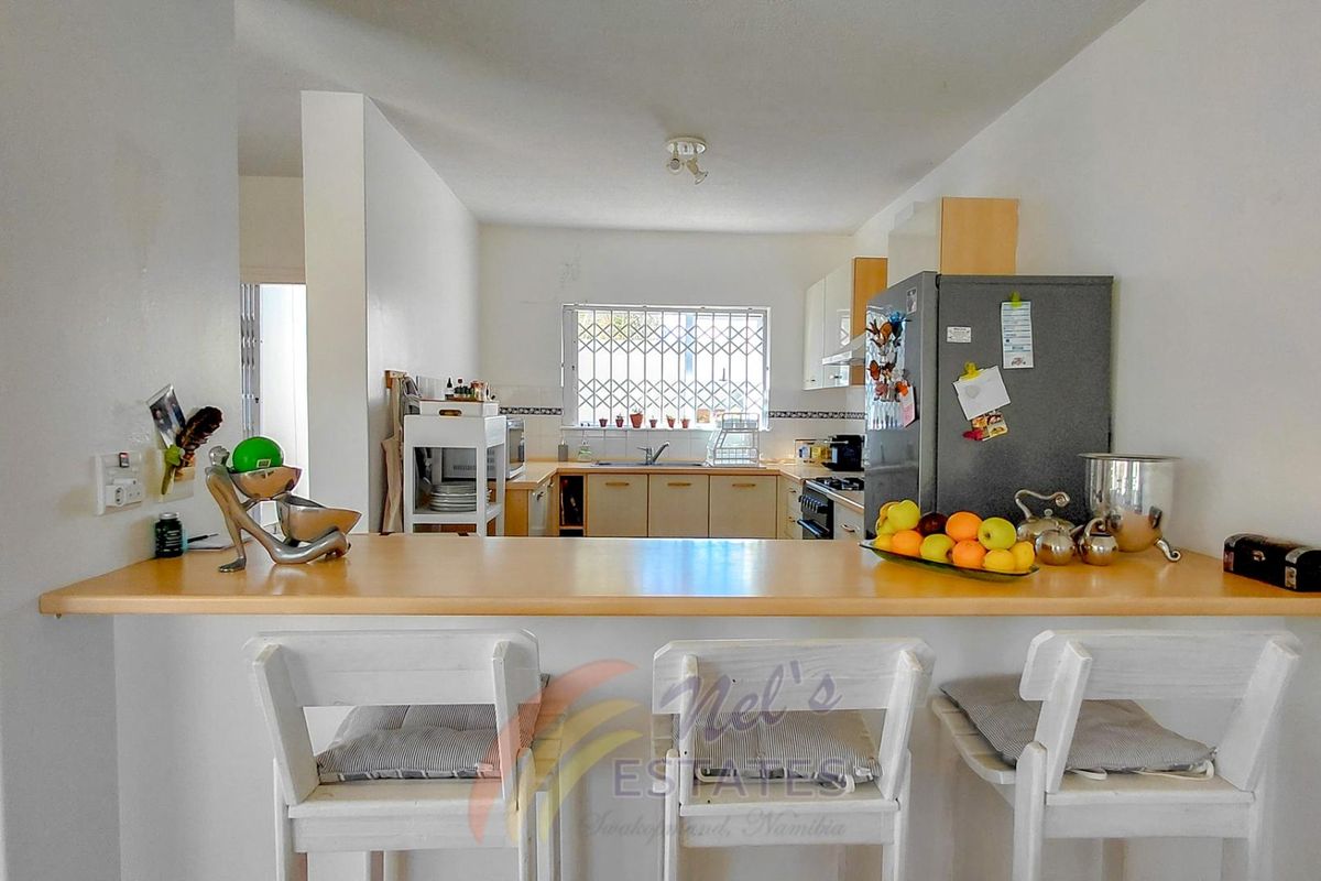 A functional kitchen featuring a breakfast bar, built-in cabinetry, and a window with security bars, overlooking the main living area.