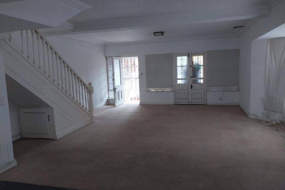 Spacious, empty living area featuring a staircase with under-stair storage, security gates, and classic ceiling cornicing, ready for renovation or staging.