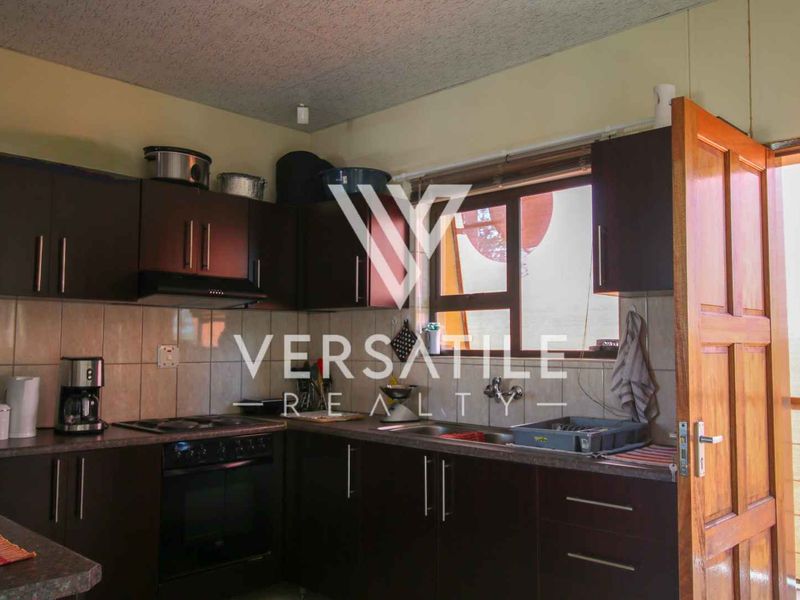 A functional kitchen featuring dark wood cabinetry, built-in oven with hob, extractor fan, and tiled backsplash, with direct access to an exterior area.