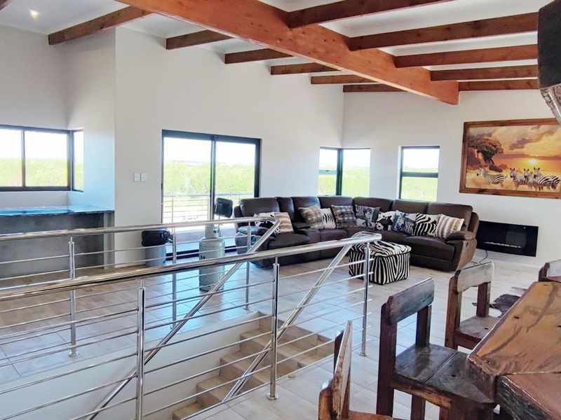 Spacious open-plan living area featuring exposed timber beams, modern stainless steel balustrades, tiled floors, and a built-in fireplace with scenic views.