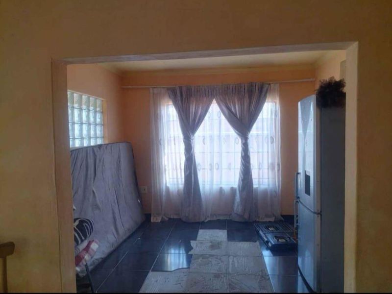 A living area featuring tiled flooring and a glass block window, currently requiring cosmetic updates and floor repairs.