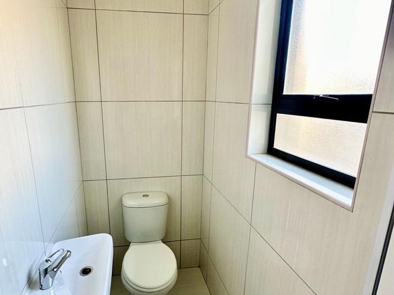 A clean, modern guest bathroom featuring floor-to-ceiling neutral tiling, a wall-mounted basin with a mixer tap, and a toilet.