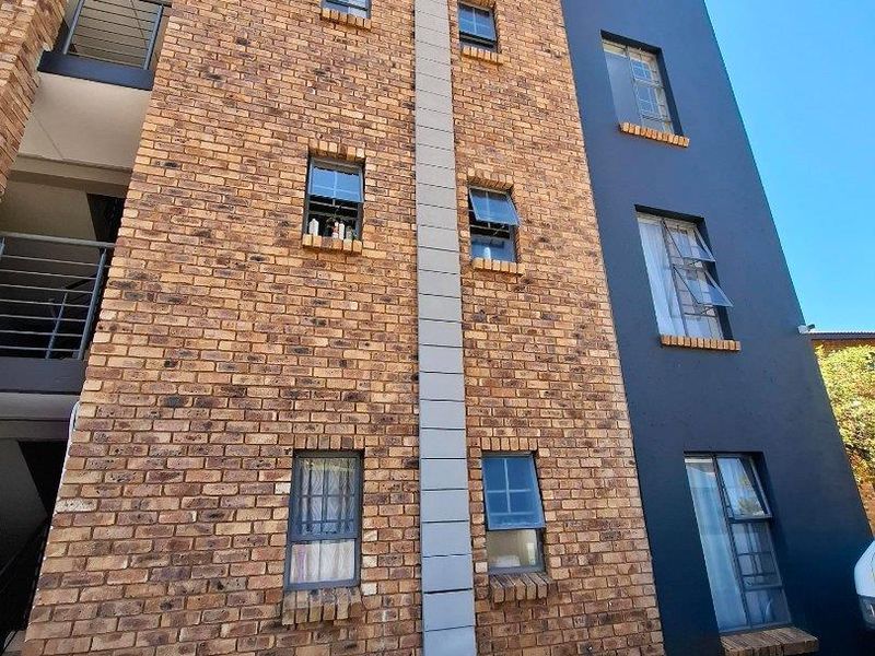 Exterior view of a multi-story apartment building featuring a combination of face brick and dark painted plaster finishes with casement windows.