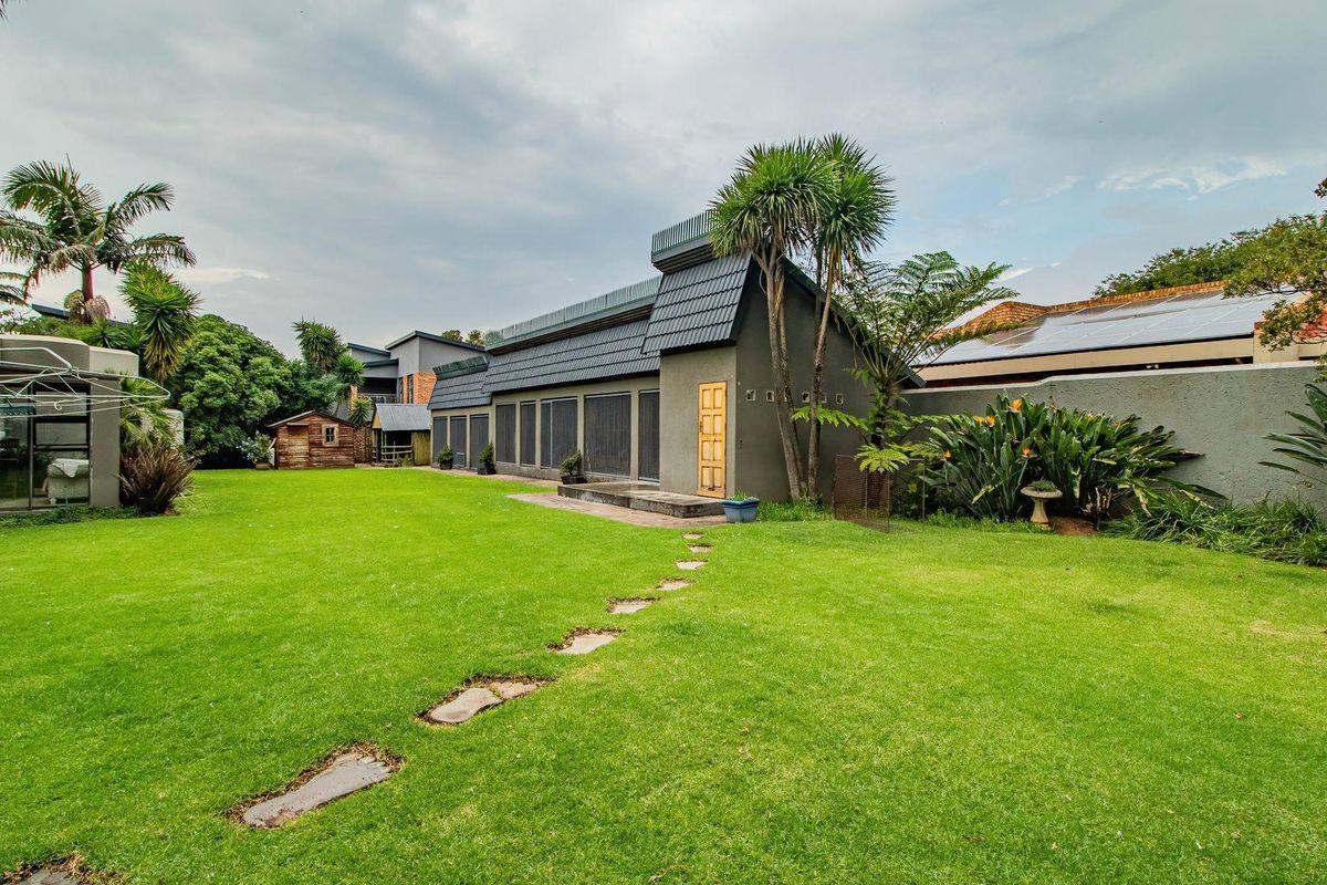 A spacious rear garden featuring a well-maintained lawn, stone pathway, and a view of the property's rear elevation with tiled roof and exterior doors.