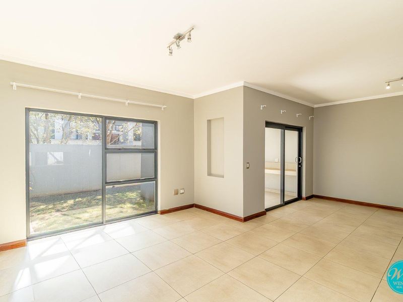Spacious, light-filled living area featuring neutral tiled flooring, modern track lighting, and large sliding glass doors providing access to the outdoor space.