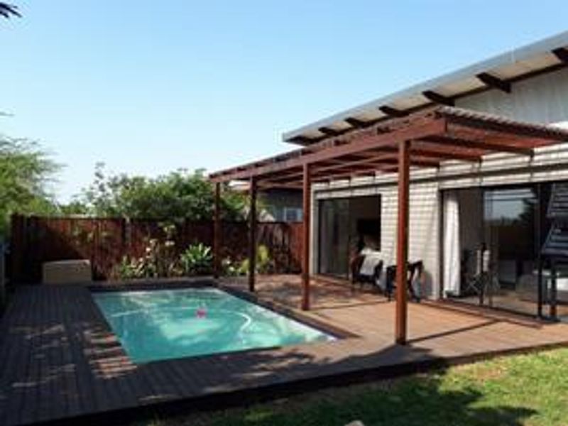 Outdoor entertainment area featuring a swimming pool, timber decking, and a wooden pergola, providing seamless access to the home through sliding glass doors.