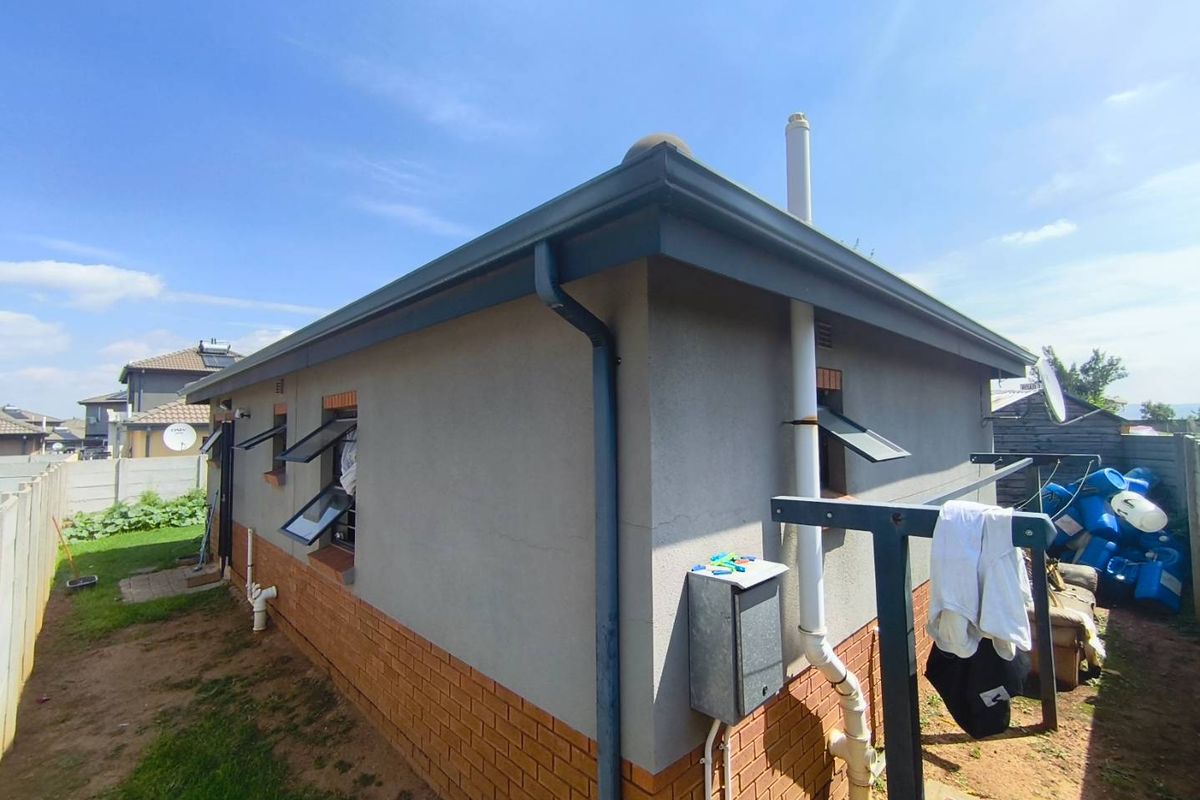Rear exterior view of the property featuring plastered walls with a brick plinth, functional gutters, and top-hung window frames.