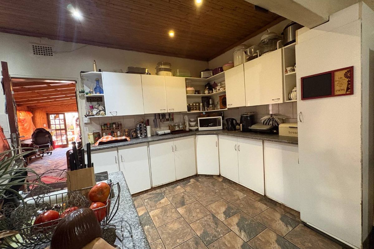 A functional kitchen featuring white cabinetry, laminate countertops, tiled flooring, and a timber-paneled ceiling, with an open transition to an adjacent living area.