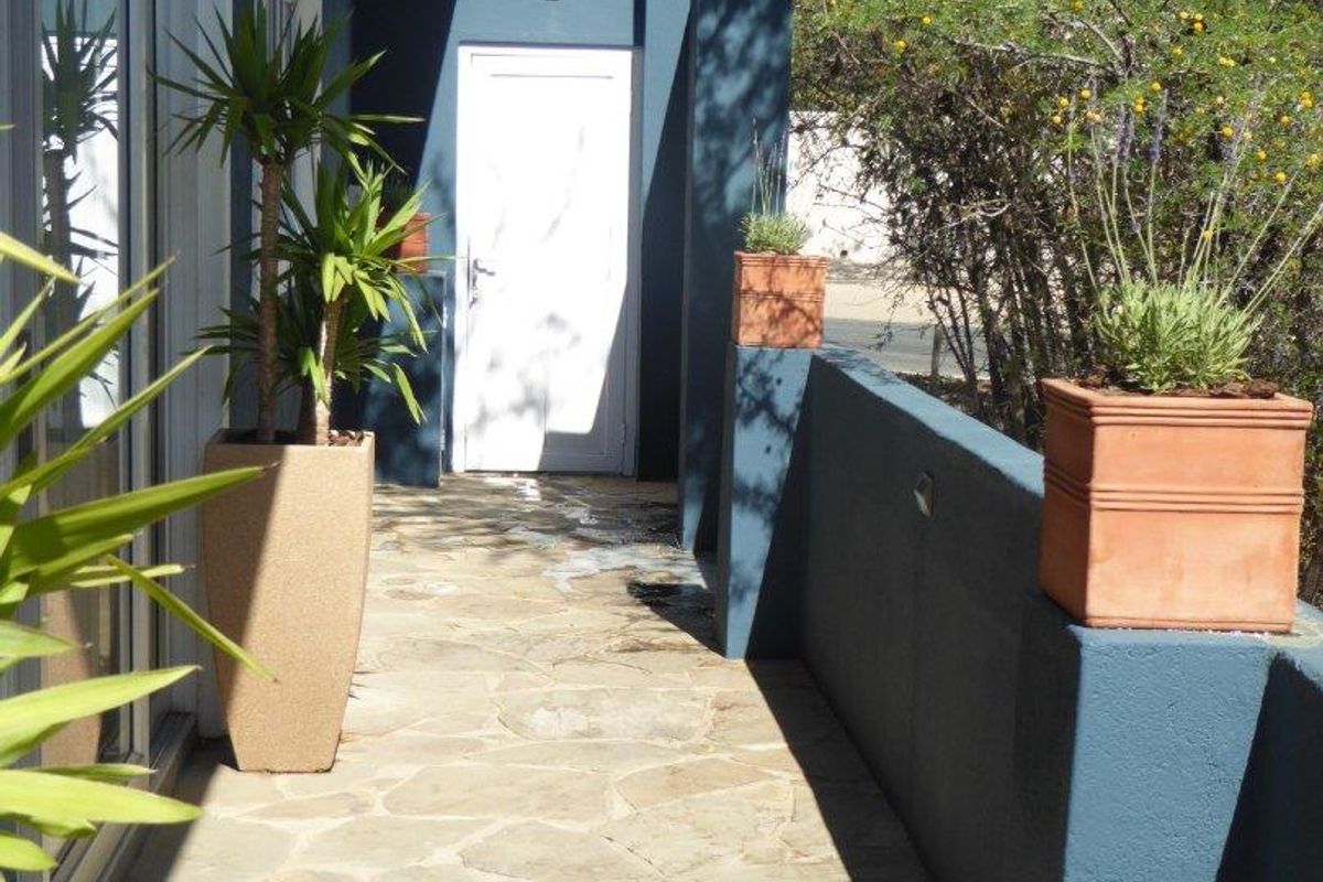 A well-maintained outdoor patio area featuring stone paving, a sliding glass door entrance, and a modern dark-painted masonry boundary wall.