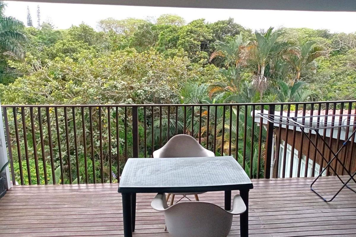 A covered balcony featuring timber decking and a metal balustrade, offering a pleasant elevated view of the surrounding lush greenery.