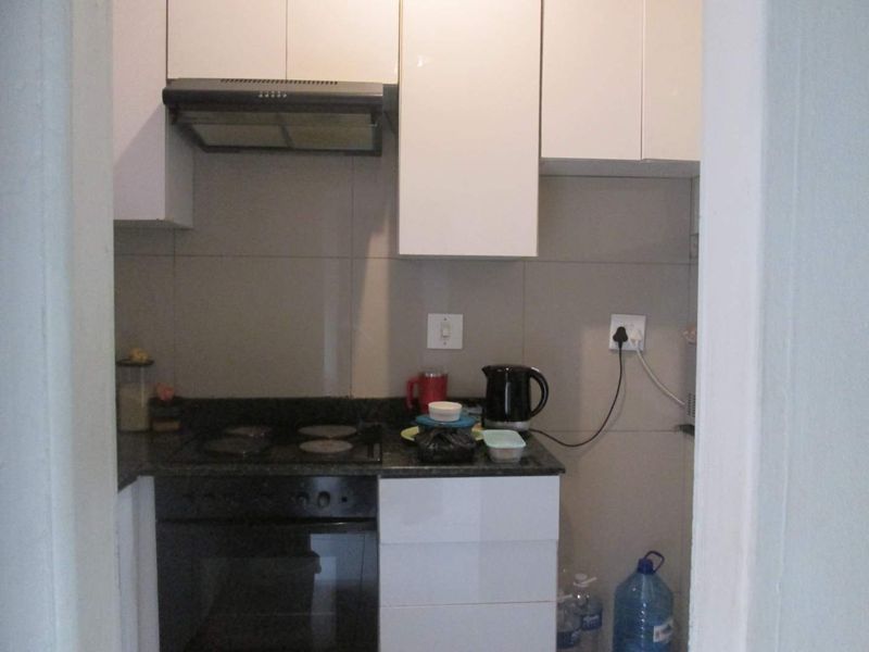 Compact kitchen featuring white cabinetry, granite countertops, a built-in oven, electric hob, and a tiled backsplash.