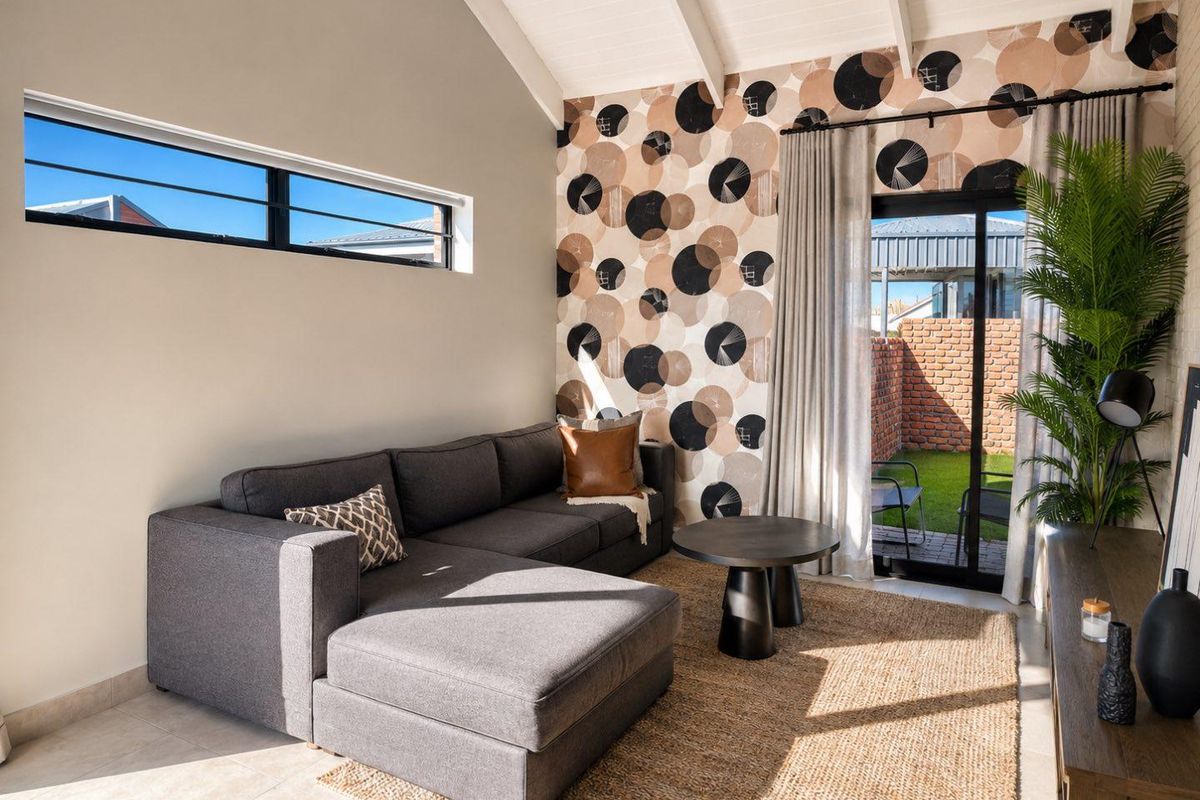 A bright living room featuring vaulted ceilings with exposed beams, large windows, and sliding glass doors providing direct access to the rear patio and garden.