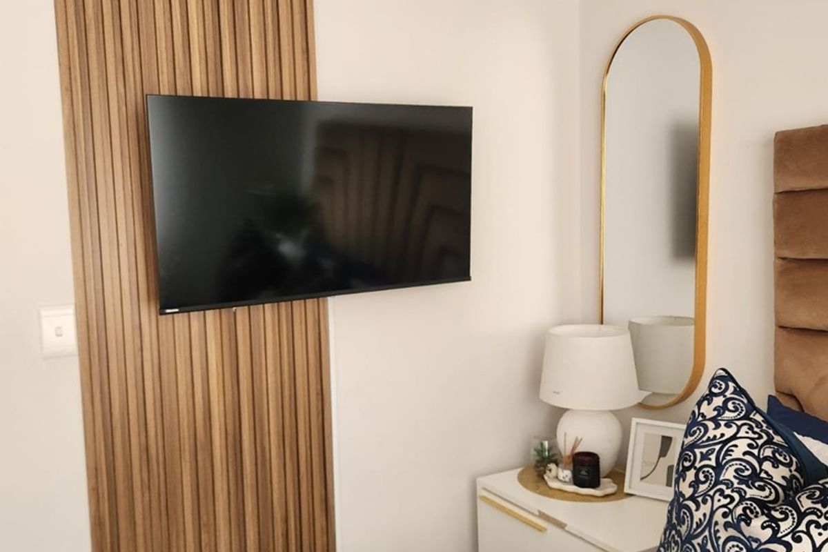 A modern bedroom featuring a decorative vertical slatted wood wall panel with a mounted television.