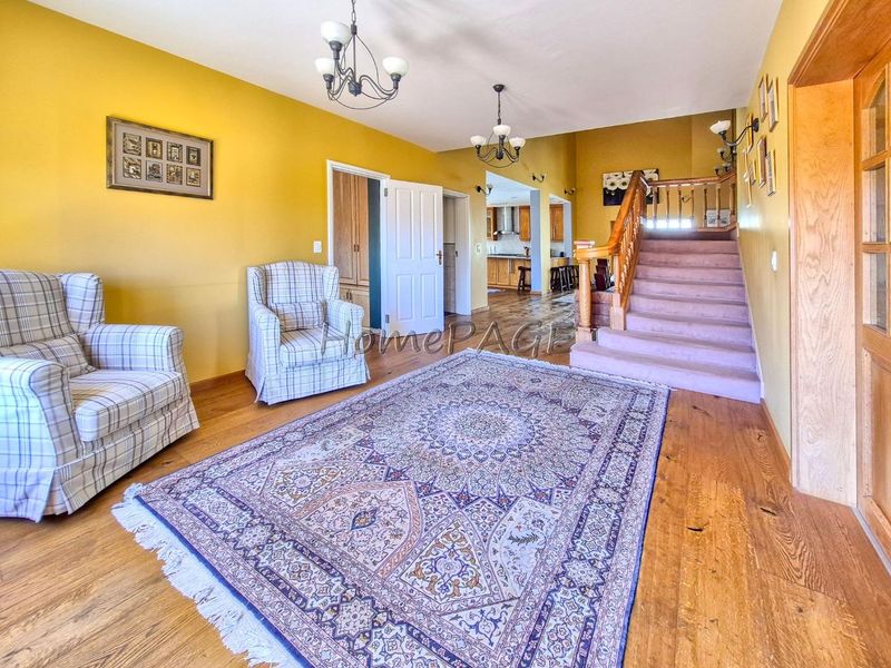 Spacious living area featuring hardwood flooring, a prominent wooden staircase with balustrade, and open access to the kitchen area.