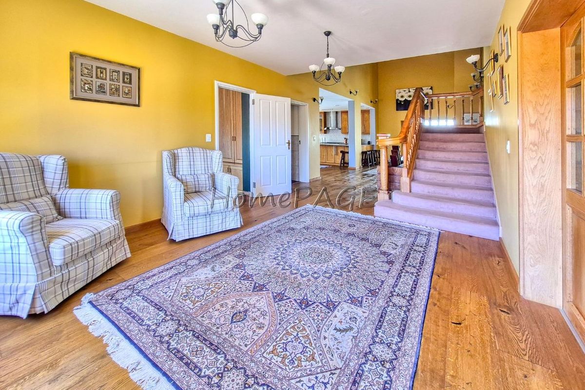 Spacious living area featuring hardwood flooring, a prominent wooden staircase with balustrade, and open access to the kitchen area.