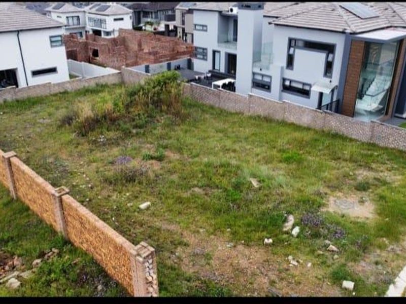 An aerial view of a vacant residential plot enclosed by perimeter walls, situated within a developed estate with neighboring modern homes.