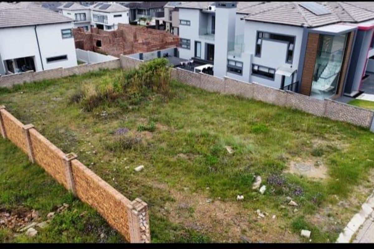 An aerial view of a vacant residential plot enclosed by perimeter walls, situated within a developed estate with neighboring modern homes.