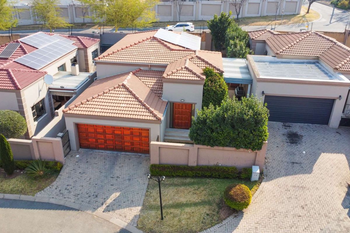 Aerial view of a residential property featuring a tiled roof, solar panels, double garage, paved driveway, and established garden within a secure estate.